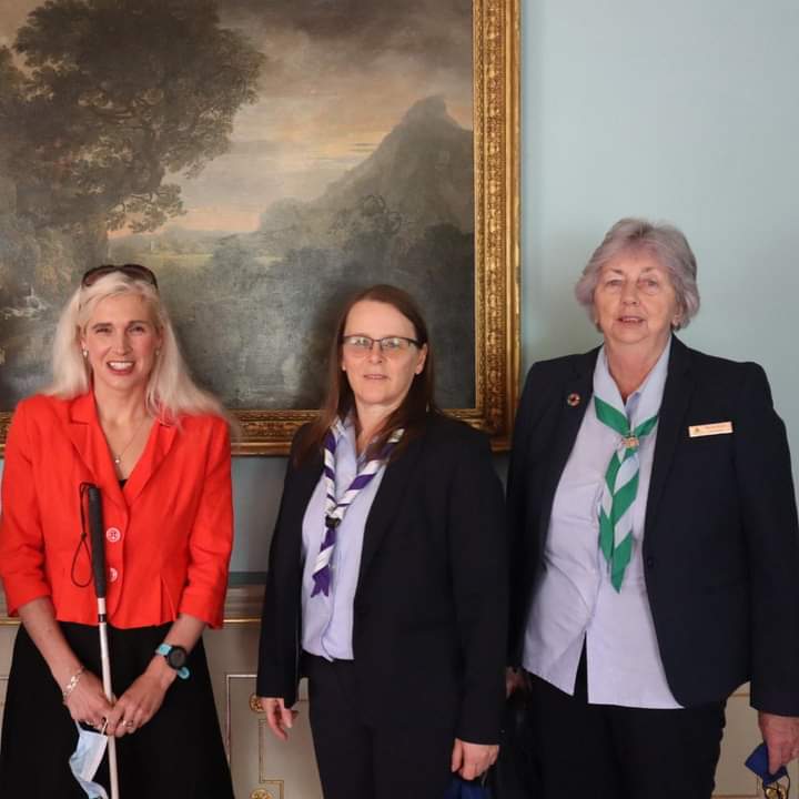 Three woman, including Irish Girl Guides Ambassador Sinead Kane, standing in front of a painting