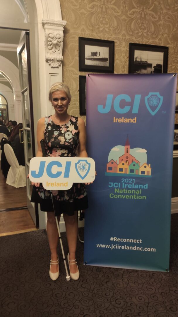 A blonde woman (Sinead Kane) holding a sign saying JCI Ireland