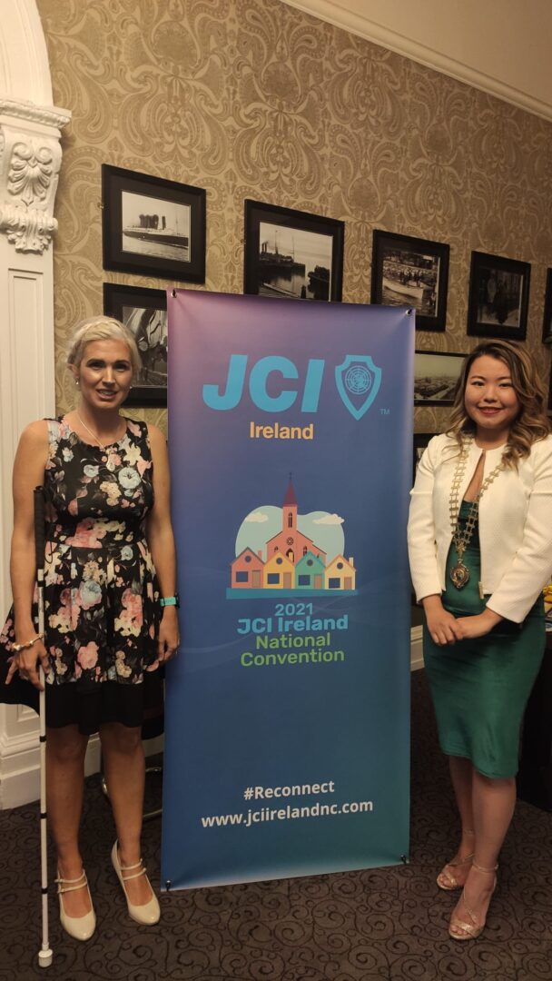 Two woman (including Sinead Kane) stood in front of a banner saying 2021 JCI Ireland National Convention