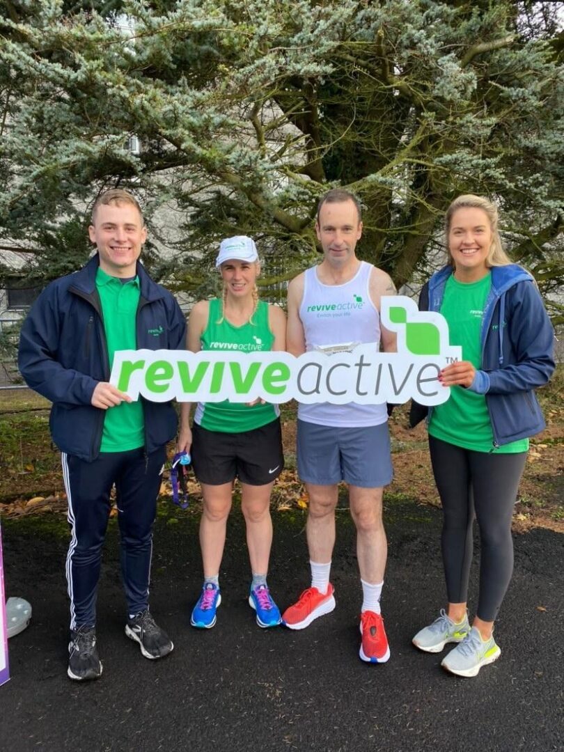 Marathon Running Coach John O'Regan and Ultra Runner Sinead Kane posing for a photo holding a Revive Active sign along with two members of the Revive Active team
